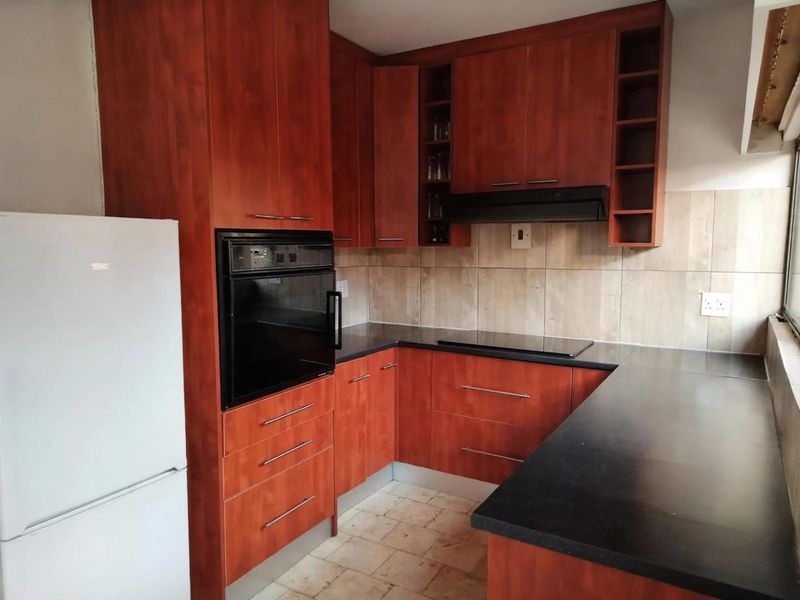 Functional kitchen featuring cherry-wood cabinetry, black laminate countertops, built-in oven, electric hob, and tiled backsplash.