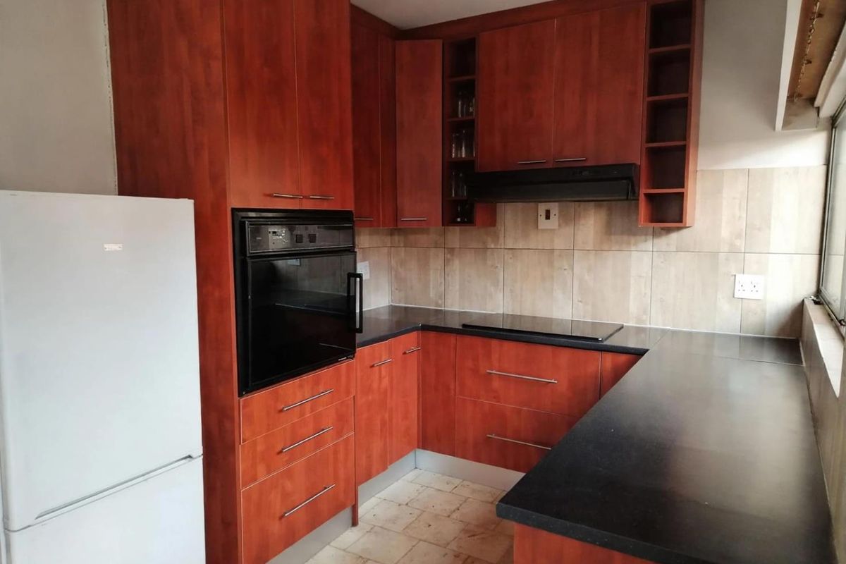 Functional kitchen featuring cherry-wood cabinetry, black laminate countertops, built-in oven, electric hob, and tiled backsplash.