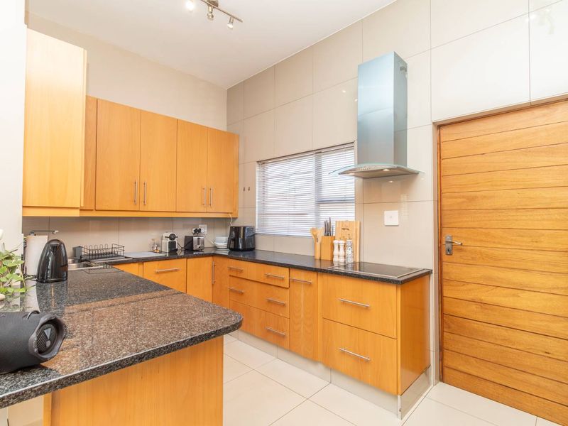 Modern kitchen featuring light wood cabinetry, granite countertops, stainless steel extractor fan, and tiled finishes throughout.