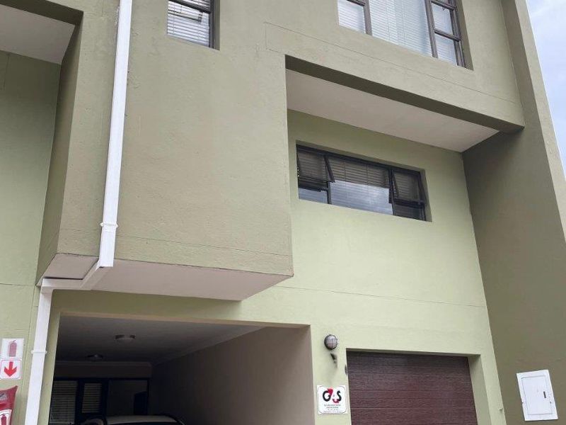Front elevation of a multi-story townhouse featuring a covered parking bay, integrated garage, and modern aluminium window frames.
