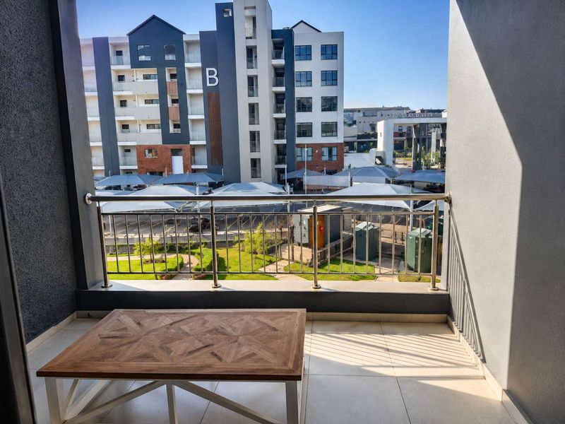 A modern balcony featuring a stainless steel balustrade and tiled flooring, offering an elevated view of the apartment complex grounds and parking area.