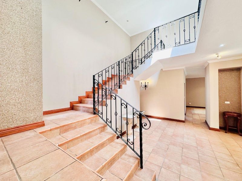 Spacious entrance hall featuring a grand staircase with decorative wrought iron balustrades and tiled flooring.