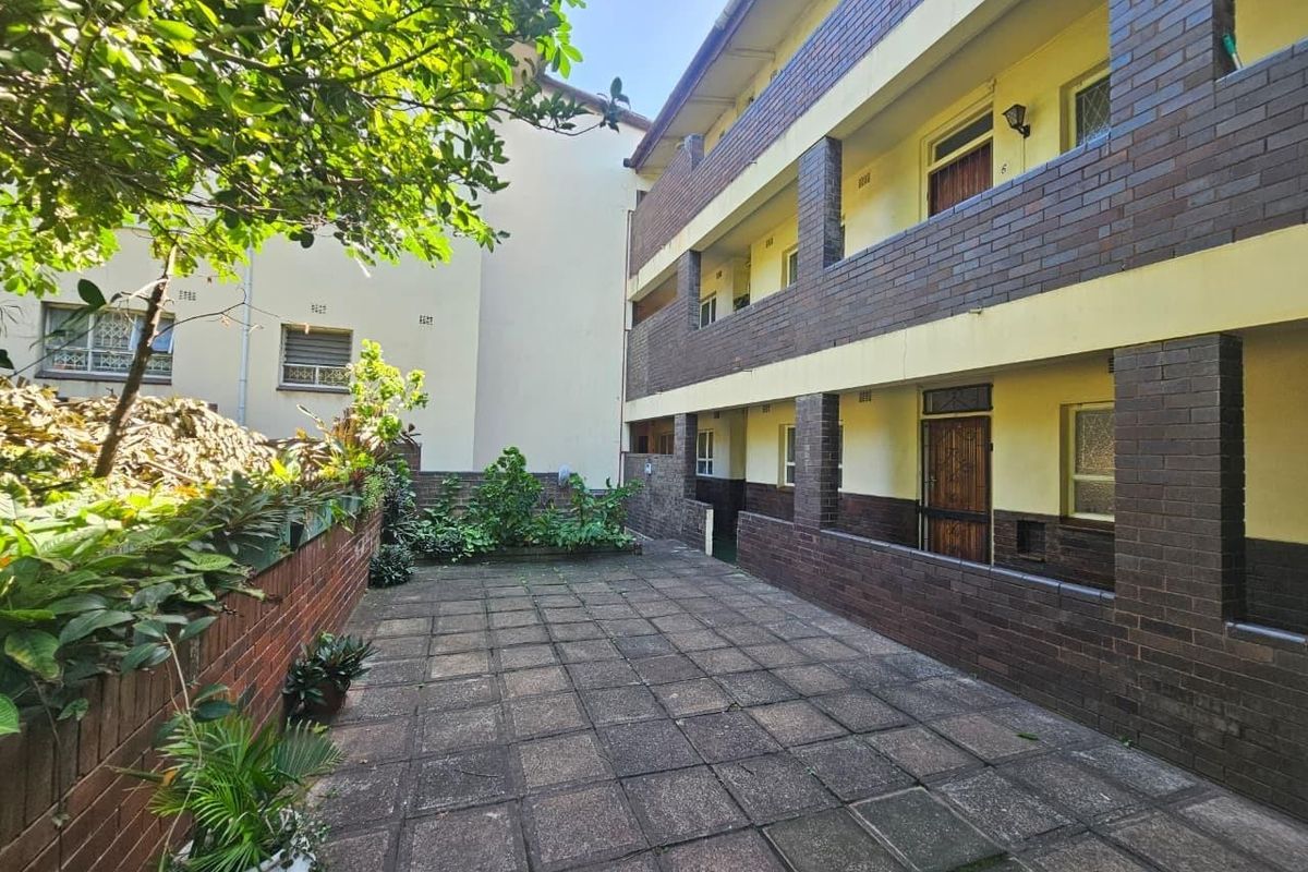 A rear courtyard area featuring paved flooring and access to apartment units with brick facade detailing.