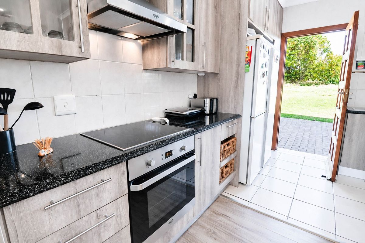 Modern kitchen featuring wood-finish cabinetry, granite countertops, integrated oven and hob, and direct access to the outdoor patio area.