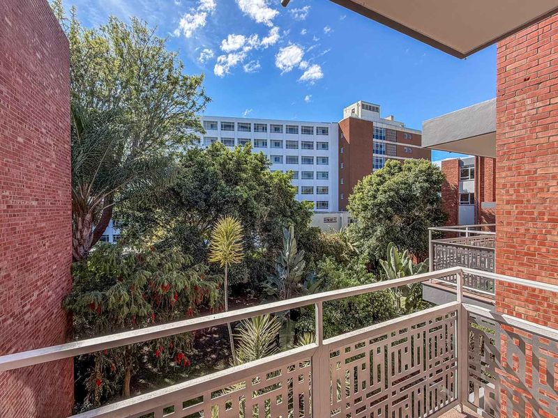 A private balcony featuring a decorative metal balustrade and views over the surrounding apartment complex gardens and mature trees.