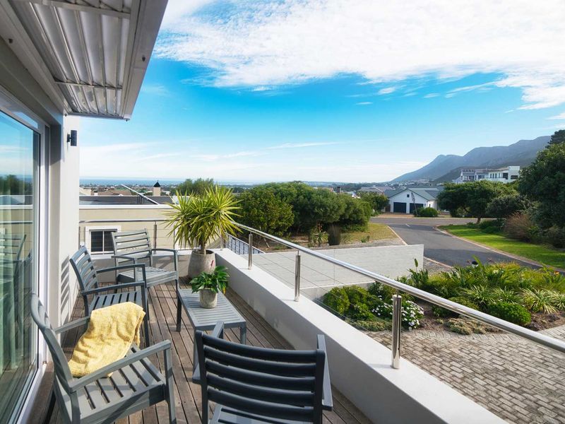 A spacious elevated balcony featuring timber decking and a modern stainless steel balustrade, offering expansive views of the surrounding neighborhood and distant mountains.