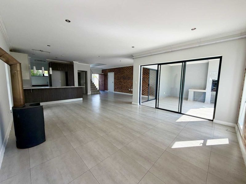 Spacious open-plan living area featuring a modern kitchen, exposed brick feature wall, freestanding fireplace, and large sliding doors leading to an outdoor patio.