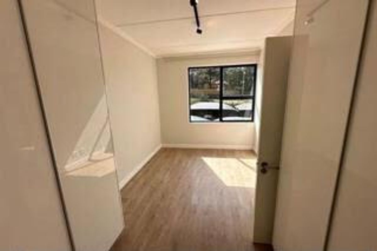 A bright, empty bedroom featuring light wood-look flooring, built-in cupboards, and a large window providing natural light.