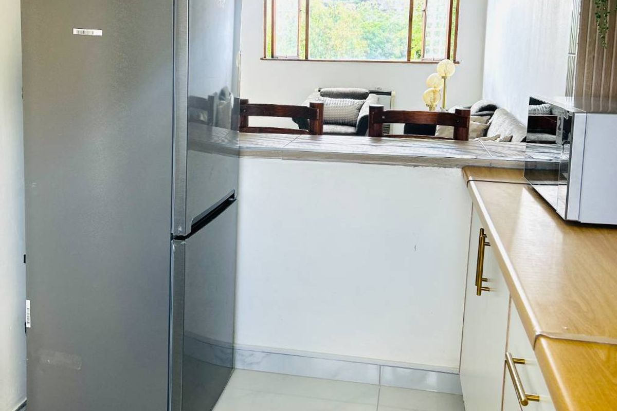 A functional kitchen featuring tiled flooring, laminate countertops, and a convenient pass-through window looking into the adjacent living area.