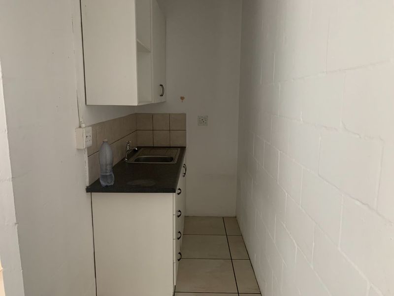A compact scullery or utility area featuring basic built-in cabinetry, a stainless steel sink, and tiled flooring, requiring cosmetic updates.