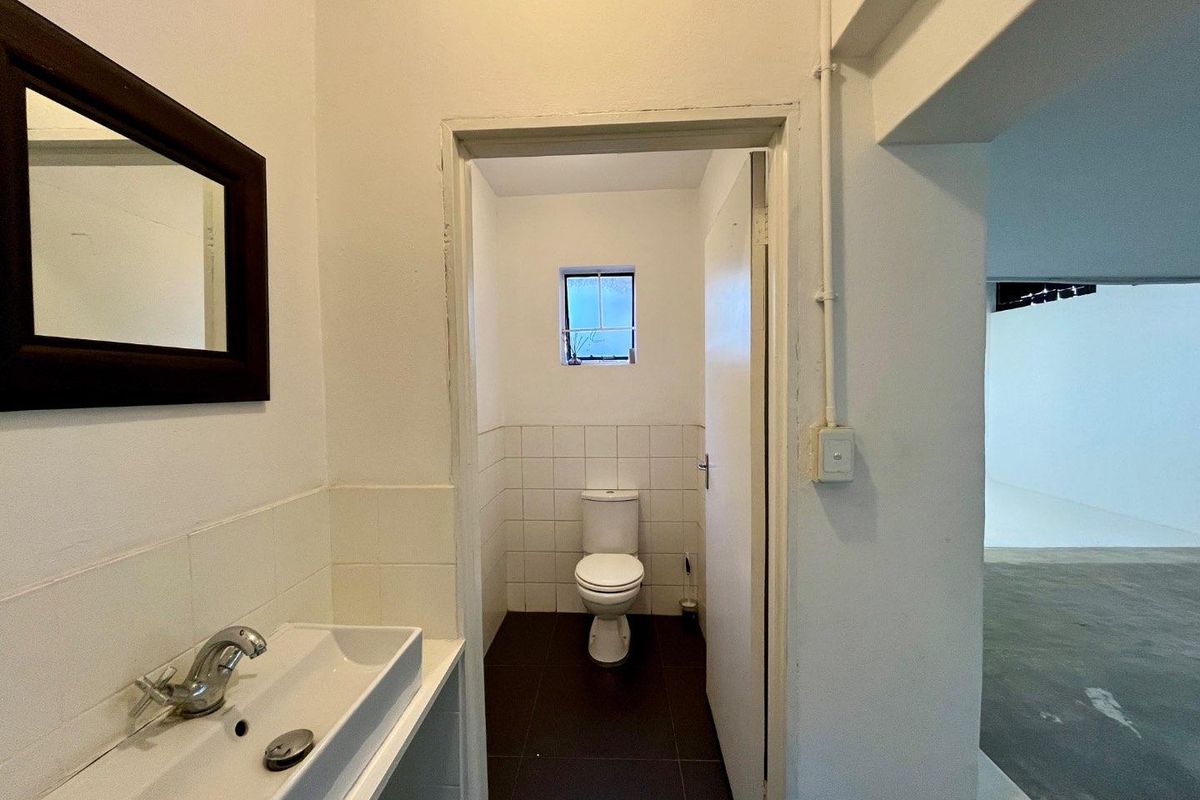 A functional bathroom featuring a wall-mounted basin and a separate toilet cubicle with tiled flooring and a small window.