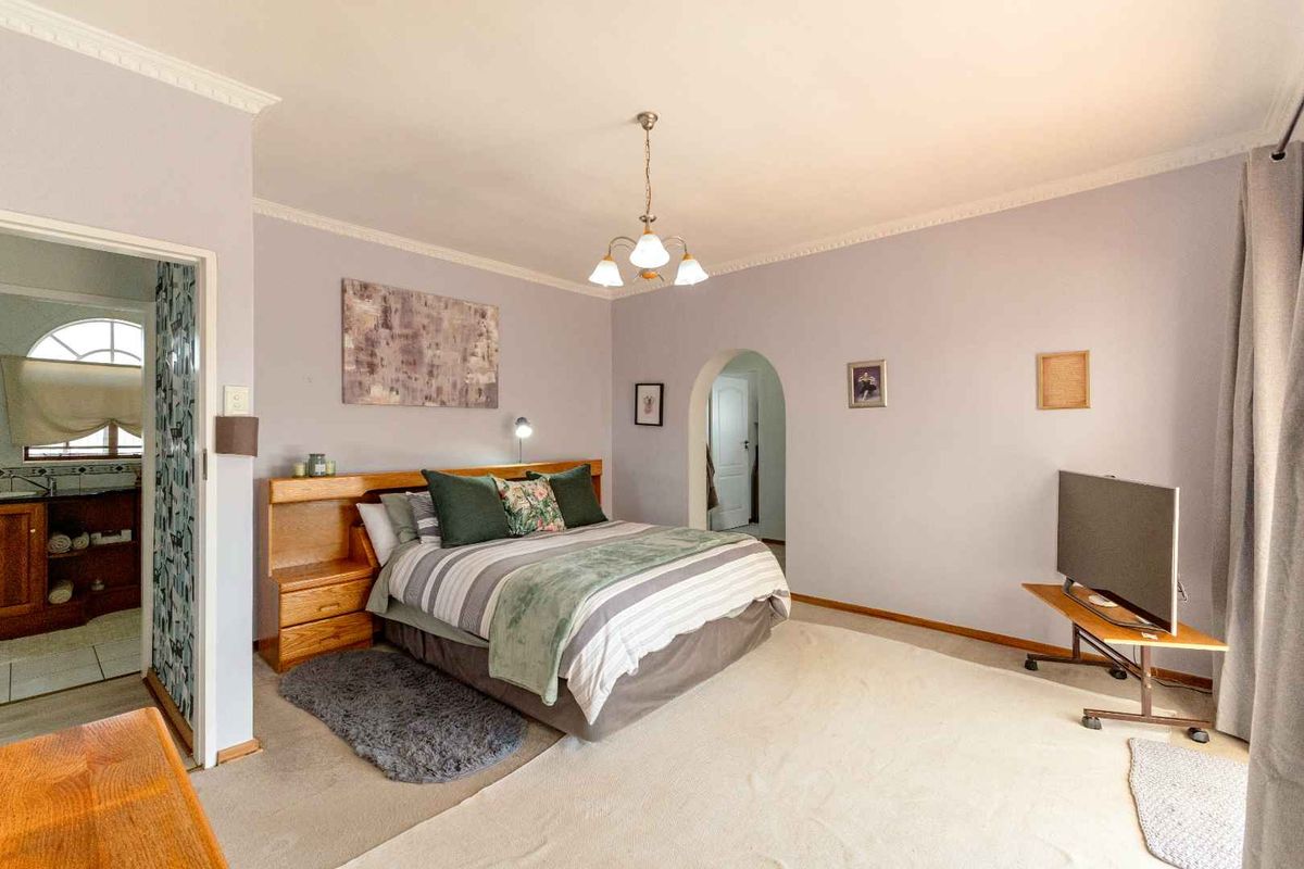 A spacious bedroom featuring neutral wall tones, crown molding, and an arched doorway leading to an adjoining bathroom.