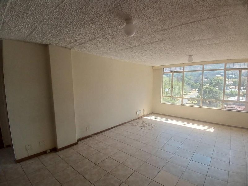 An empty, sunlit living area featuring tiled flooring, a textured ceiling, and large windows offering an elevated view.