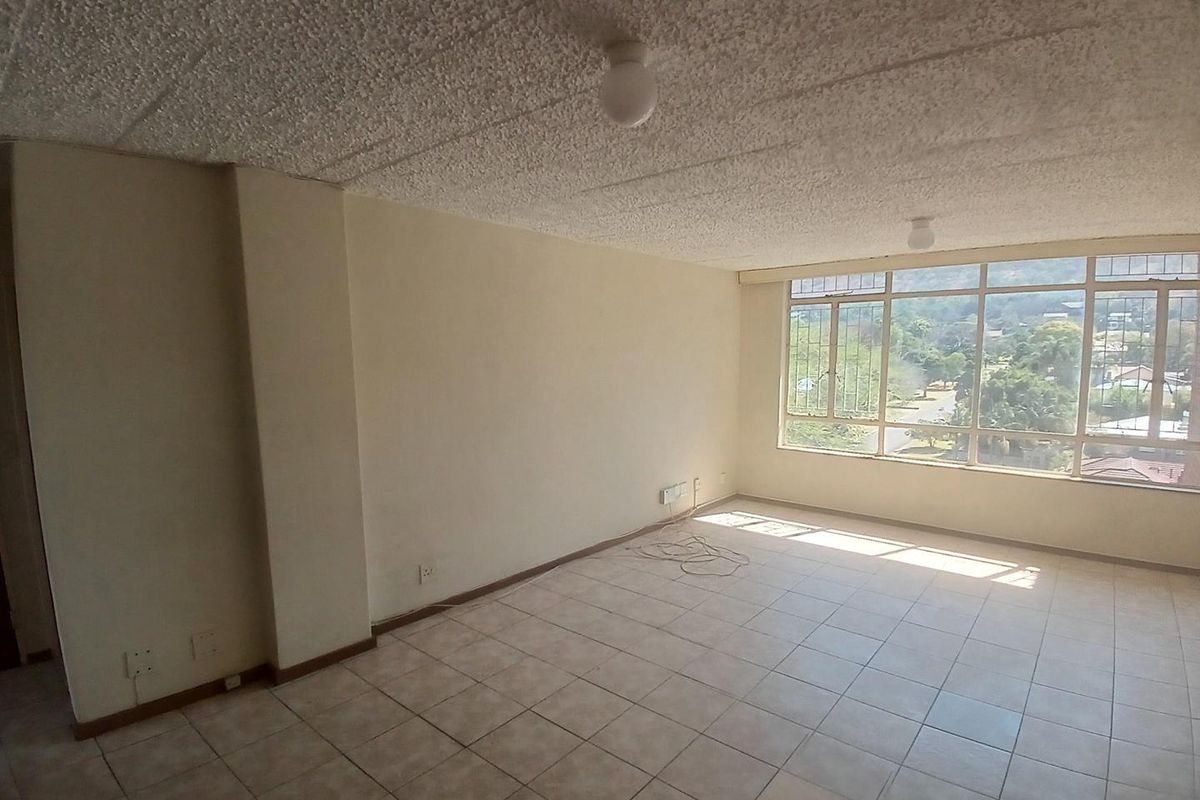 An empty, sunlit living area featuring tiled flooring, a textured ceiling, and large windows offering an elevated view.