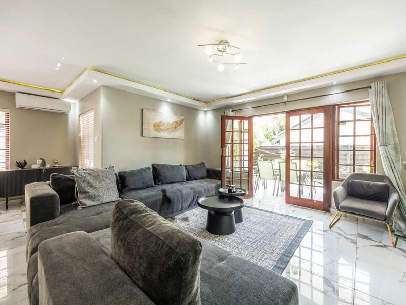 A bright and modern living room featuring polished marble-look flooring, recessed ceiling lighting, and timber-framed french doors providing seamless access to the outdoor patio area.