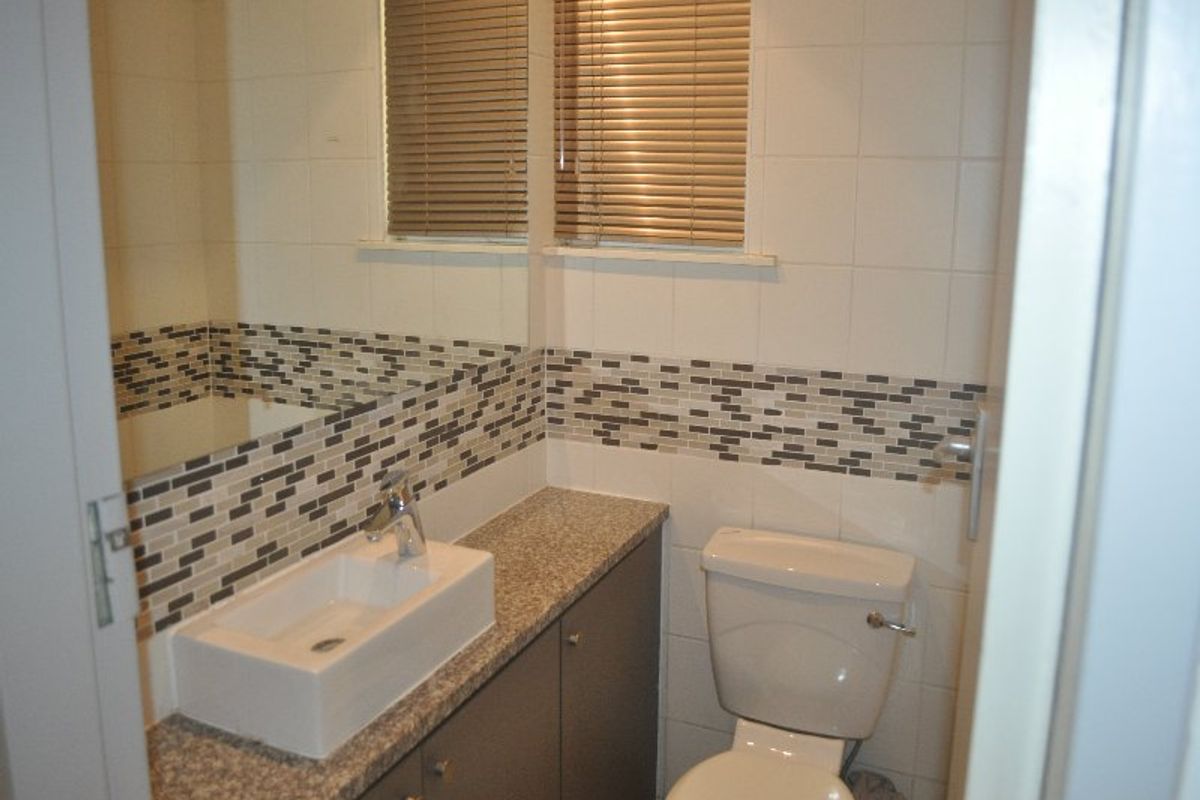 A compact bathroom featuring a vanity with a granite countertop, vessel sink, mosaic tile backsplash, and a wall-mounted mirror.