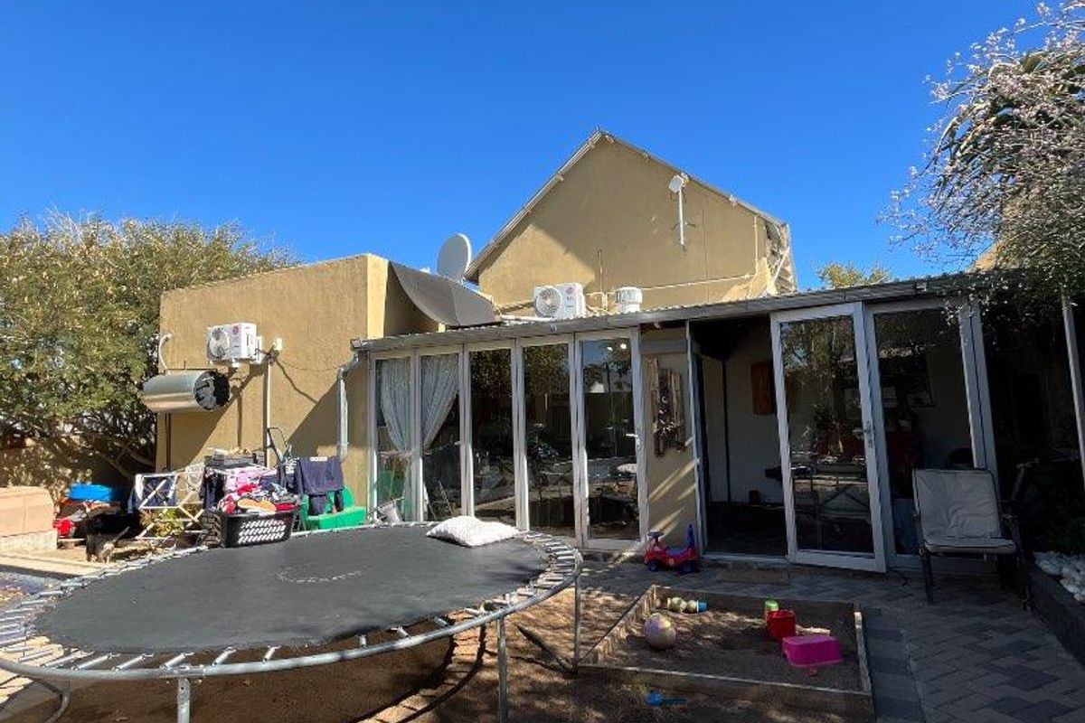 Rear exterior view of the house featuring sliding glass doors, paved patio area, and external wall-mounted utility fixtures.