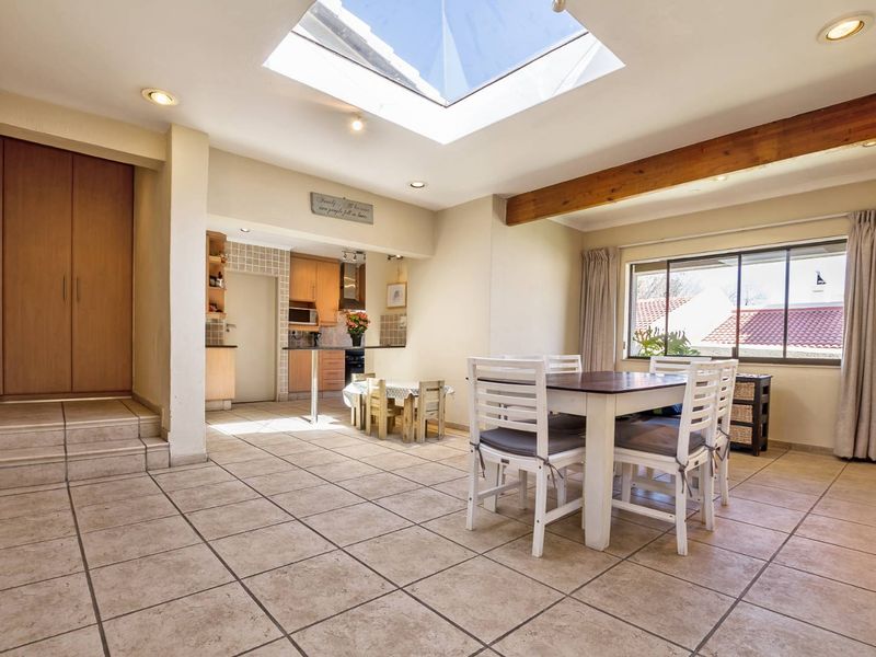 Spacious open-plan living and dining area featuring a large skylight, tiled flooring, and an exposed timber beam, seamlessly connecting to the kitchen.