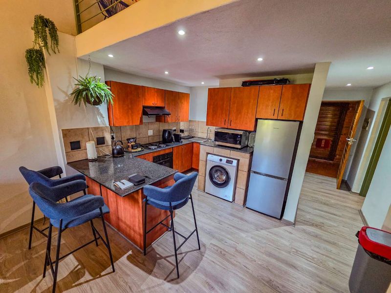 Compact kitchen featuring wood-finish cabinetry, granite countertops, integrated appliances, and a breakfast bar, illuminated by recessed downlights.