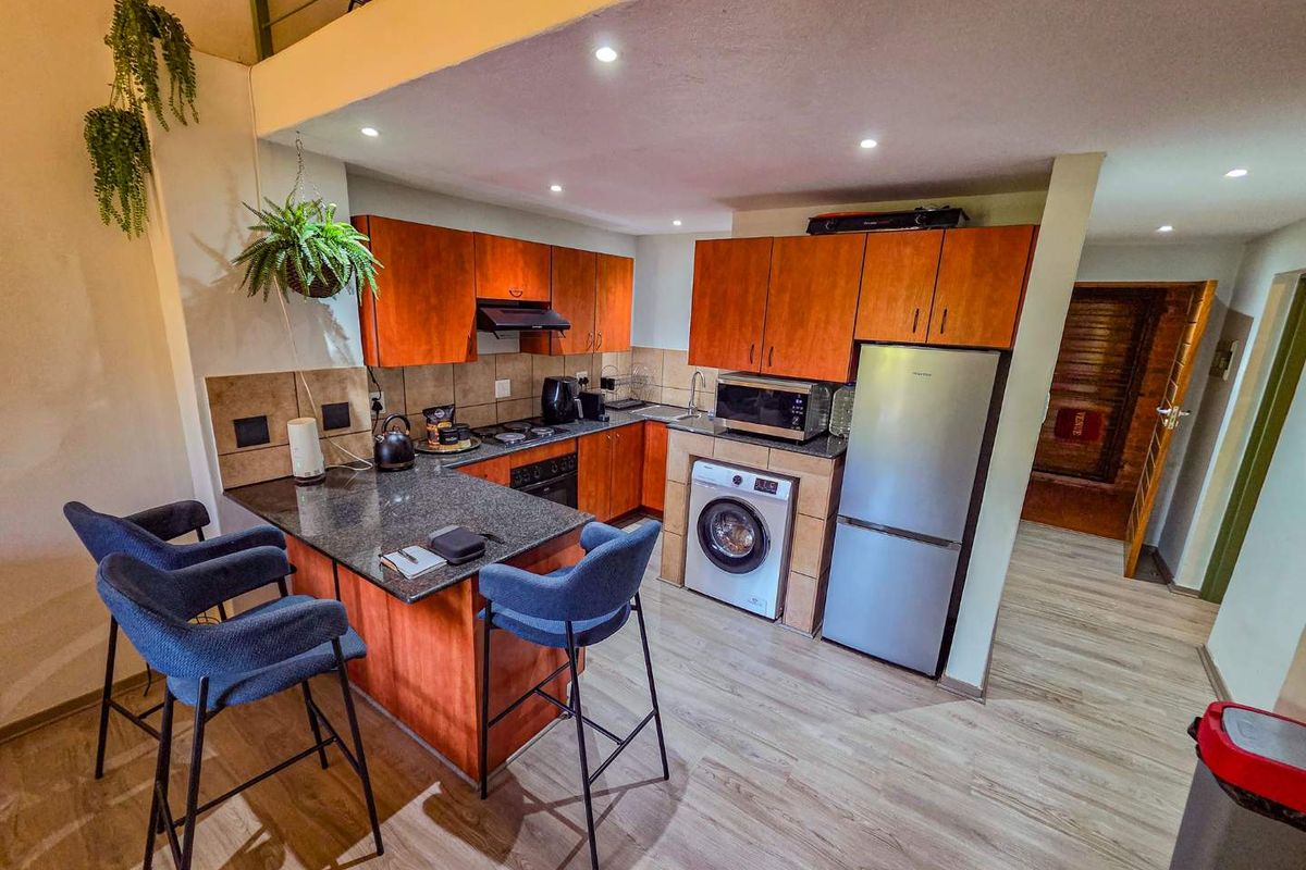 Compact kitchen featuring wood-finish cabinetry, granite countertops, integrated appliances, and a breakfast bar, illuminated by recessed downlights.