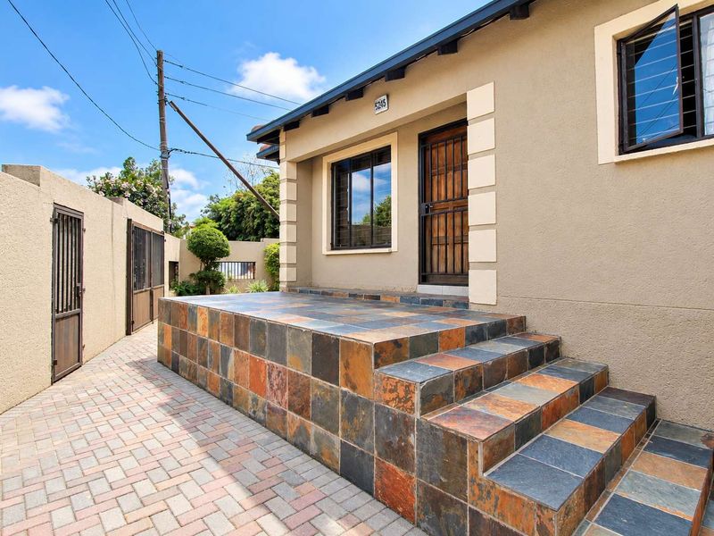 Front entrance of the house featuring a raised tiled porch, paved driveway, and secure metal gate access.