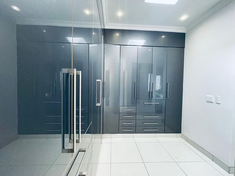 A modern bedroom featuring high-gloss grey built-in cupboards, sleek tiled flooring, and recessed ceiling lighting in a clean, minimalist space.