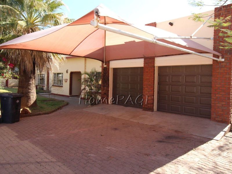 Front exterior view featuring a double garage with brick pillars and a large shade sail covering the paved driveway area.