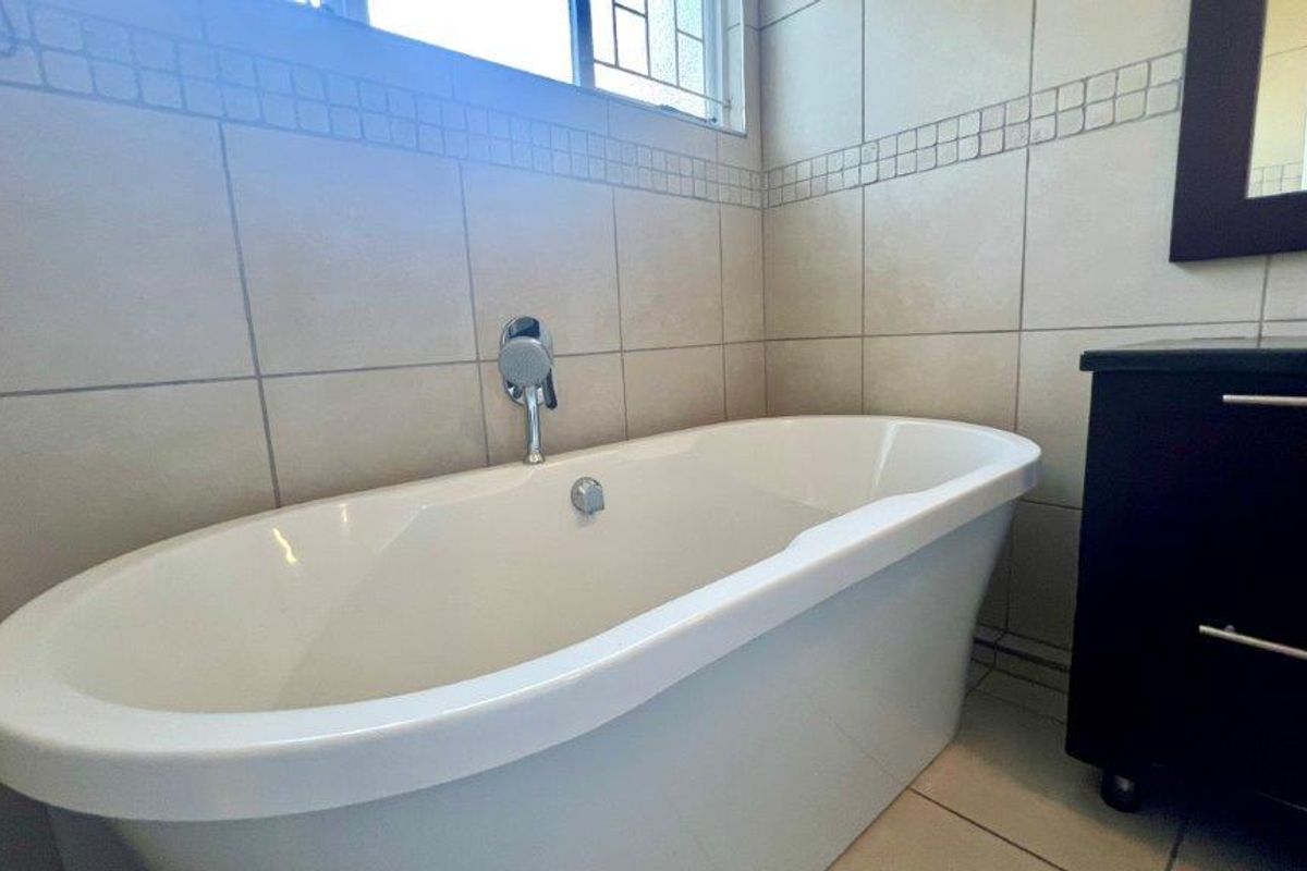 A modern bathroom featuring a clean white freestanding bathtub, neutral wall tiling, and a functional vanity unit.
