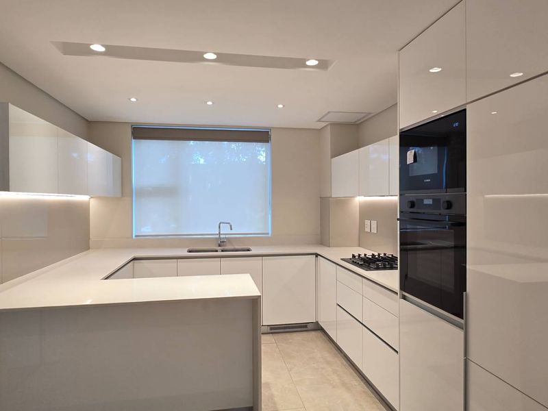 Modern, U-shaped kitchen featuring high-gloss white cabinetry, quartz countertops, integrated appliances, and recessed lighting in a clean, contemporary finish.