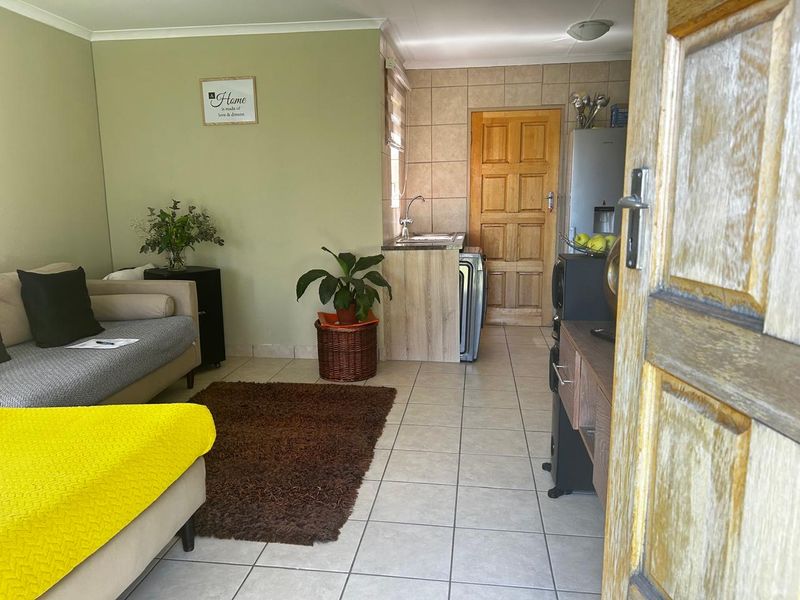 An open-plan living area featuring tiled flooring and a compact kitchenette with built-in cabinetry and sink.