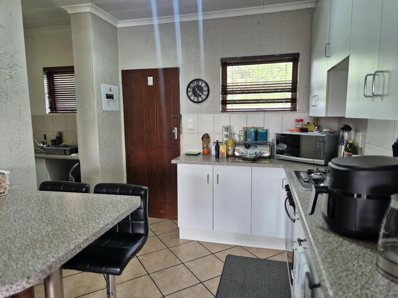 A functional kitchen featuring built-in cabinetry, stone-look countertops, a gas hob, and tiled flooring, with an adjacent scullery area visible.