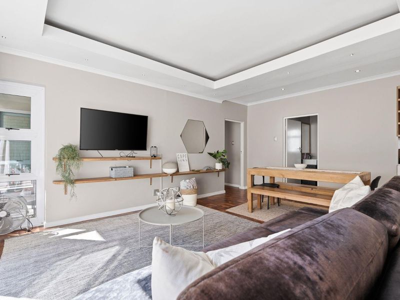 Spacious open-plan living area featuring a recessed ceiling with downlights, hardwood flooring, and built-in shelving, creating a bright and modern atmosphere.