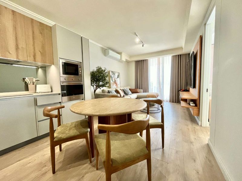 Modern open-plan living area featuring a sleek kitchen with integrated appliances, light wood-look flooring, and a wall-mounted media console.