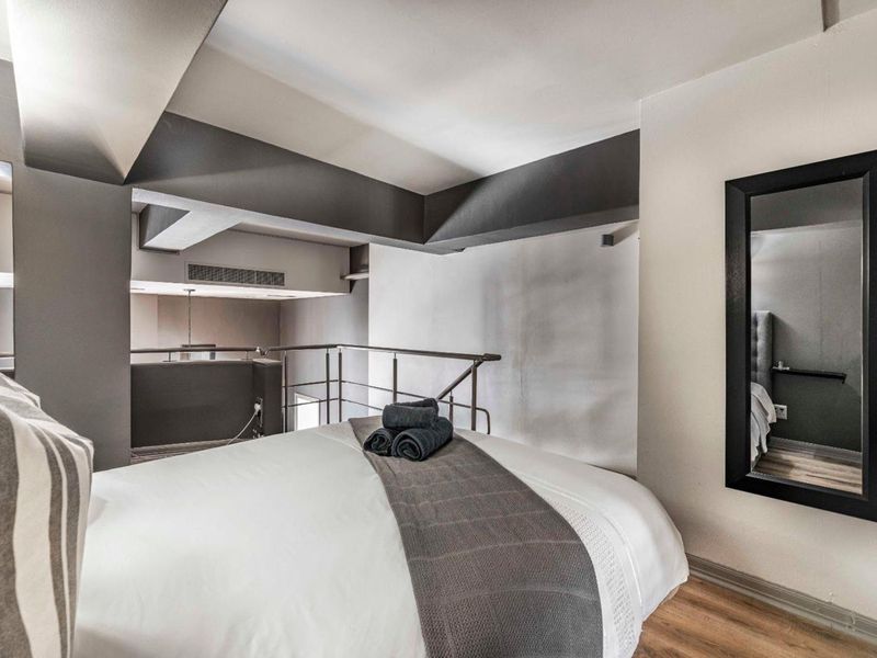 A modern mezzanine bedroom featuring laminate flooring, a metal safety balustrade, and integrated air conditioning ventilation.