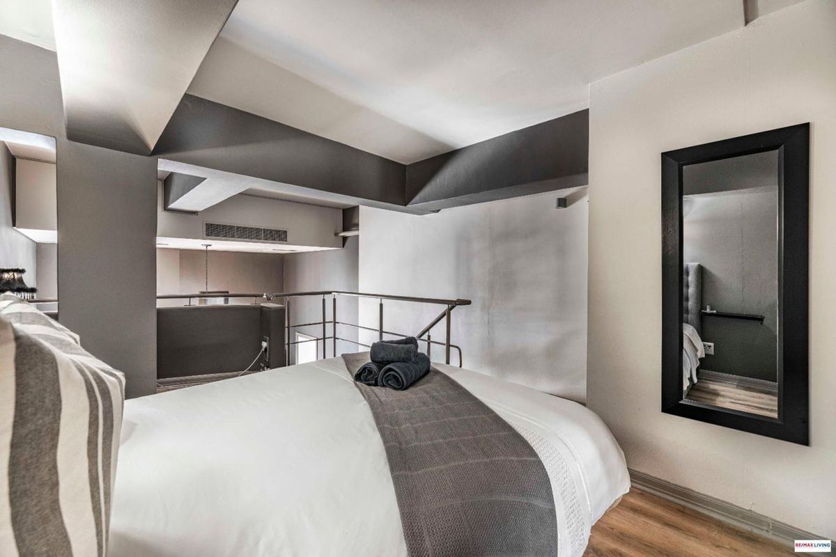 A modern mezzanine bedroom featuring laminate flooring, a metal safety balustrade, and integrated air conditioning ventilation.