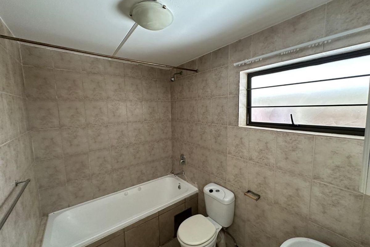 A functional bathroom featuring a bathtub, toilet, and tiled finishes throughout, offering a blank canvas for potential modern updates.