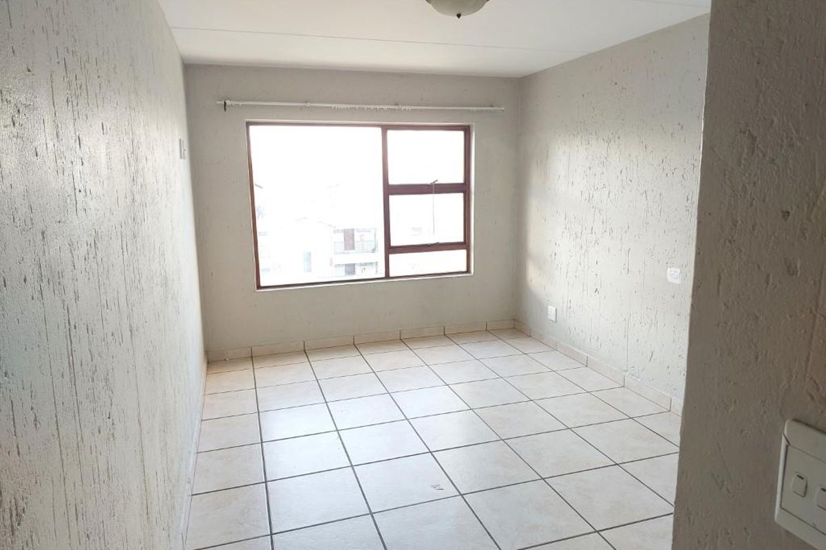 An empty bedroom featuring tiled flooring, textured walls, and a large window, providing a blank canvas for personalization.