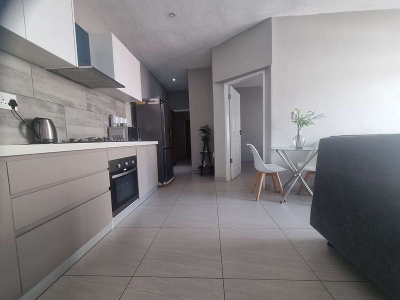 Modern open-plan kitchen featuring sleek cabinetry, built-in oven, gas hob, and neutral tiled flooring, seamlessly flowing into the living area.