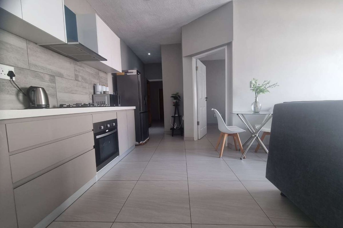 Modern open-plan kitchen featuring sleek cabinetry, built-in oven, gas hob, and neutral tiled flooring, seamlessly flowing into the living area.