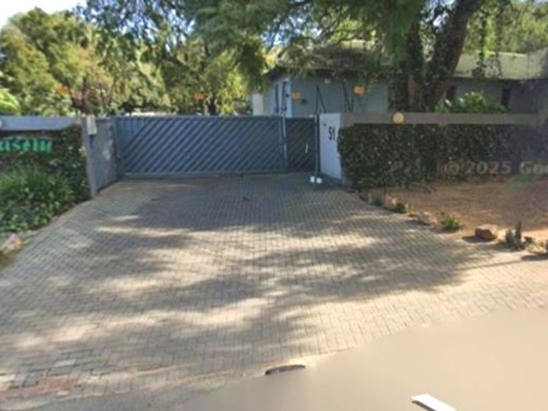 Front entrance view of the property featuring a paved driveway, secure sliding gate, and perimeter wall with established garden landscaping.