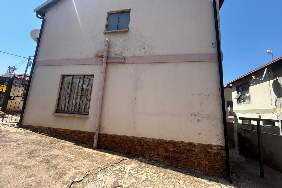 Side elevation of the house showing exterior wall with visible plaster cracking, weathered brick base, and concrete driveway surface.