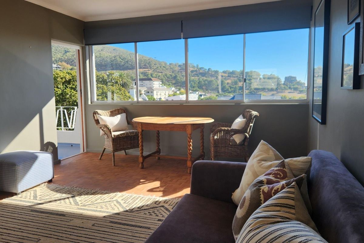 A bright living room featuring parquet flooring, large windows with scenic views, and direct access to an outdoor balcony area.