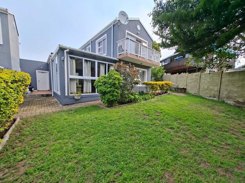 Rear view of the property featuring a small garden, paved walkway, and an upper-level balcony with a satellite dish.