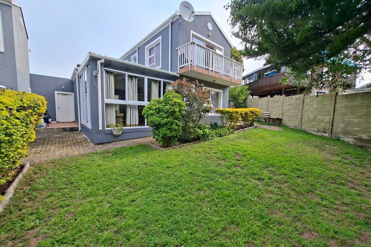 Rear view of the property featuring a small garden, paved walkway, and an upper-level balcony with a satellite dish.