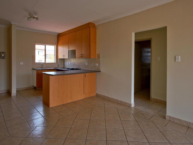 An open-plan kitchen and living area featuring tiled flooring, wooden cabinetry, and a functional layout, presented in a clean, vacant condition.