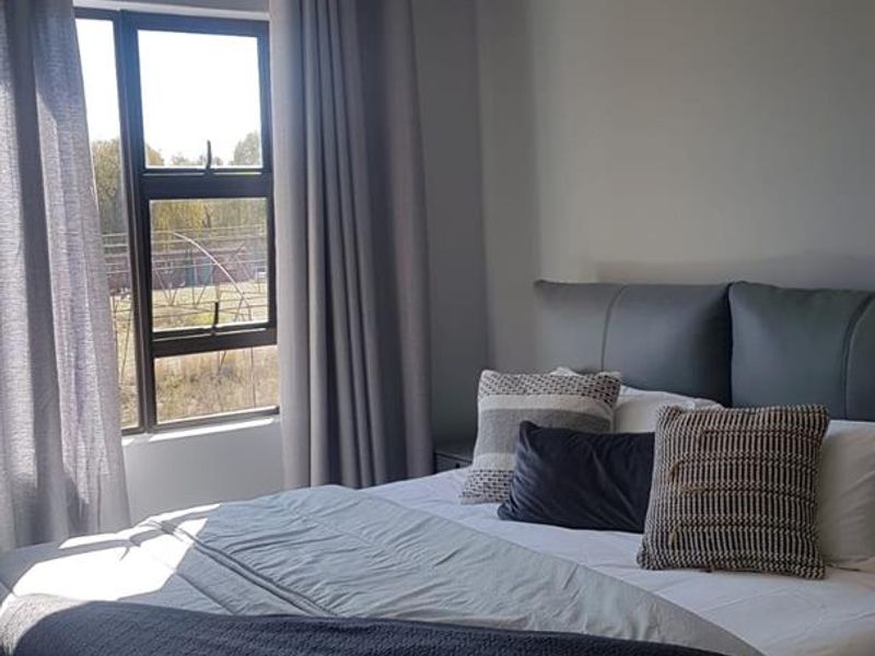 A well-lit bedroom featuring neutral grey walls, tiled flooring, and an aluminium-framed window with curtains.
