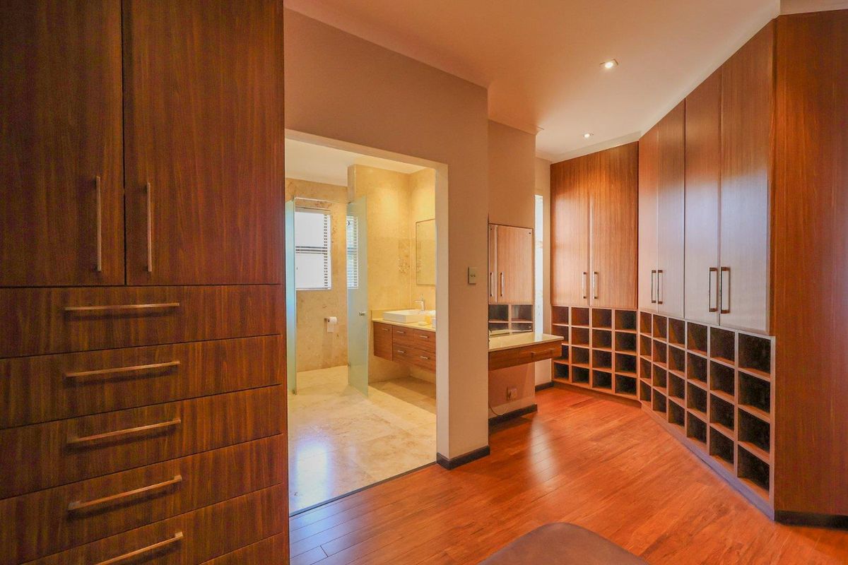 A spacious walk-in dressing room featuring extensive custom wood cabinetry and shelving, leading directly into a modern en-suite bathroom with stone tiling.