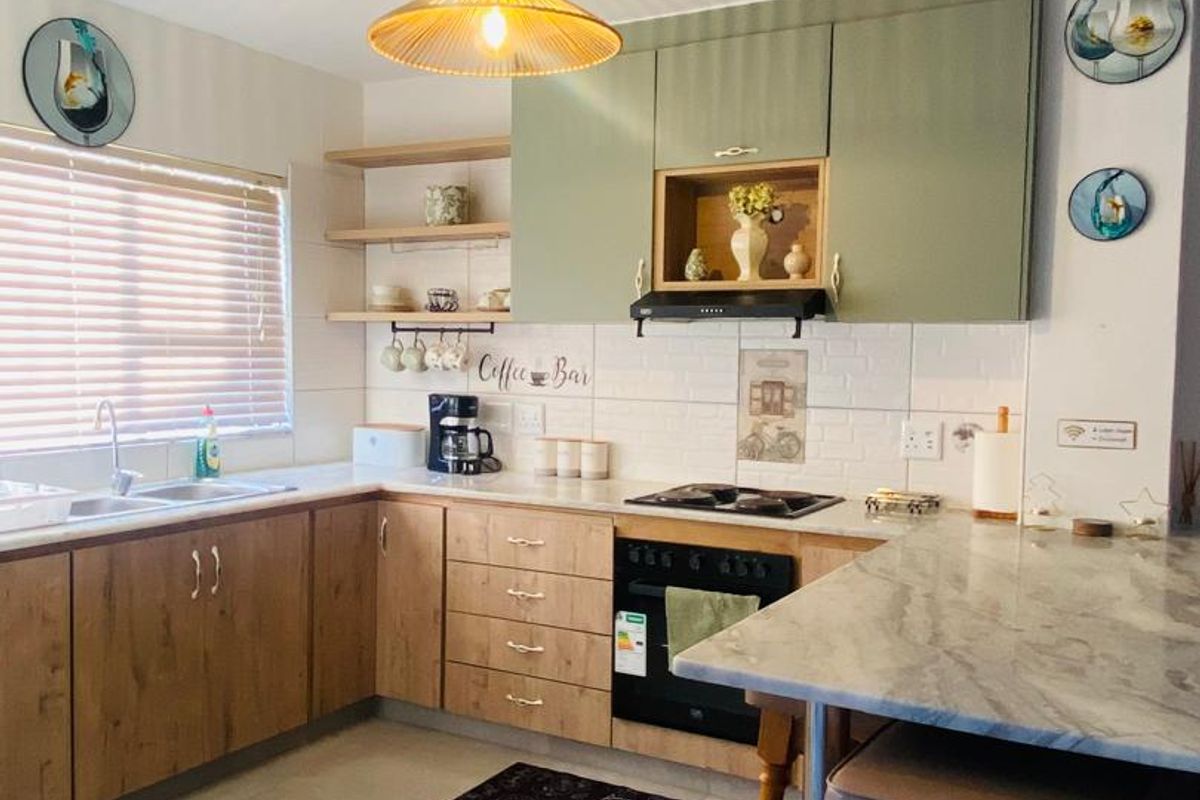 Modern kitchen featuring wood-tone and sage green cabinetry, stone countertops, integrated oven, hob, and a functional breakfast bar area.