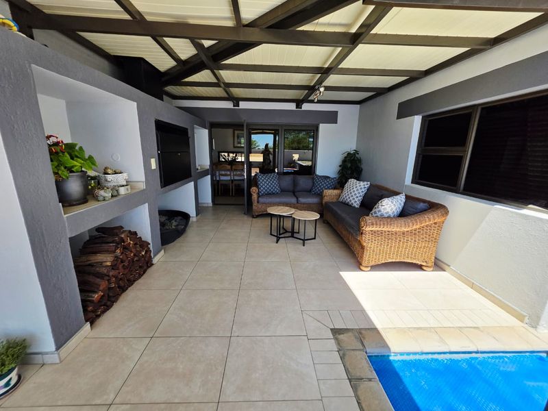 A spacious covered patio featuring a built-in braai, tiled flooring, and direct access to an adjacent swimming pool.
