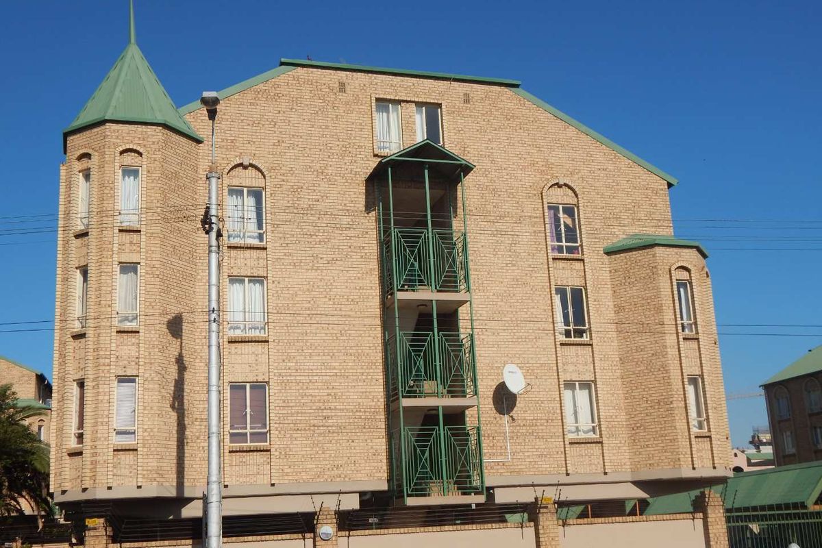 Front elevation of a multi-story apartment building featuring face brick construction, green metal roofing, turret architectural detail, and stacked balconies with metal railings.